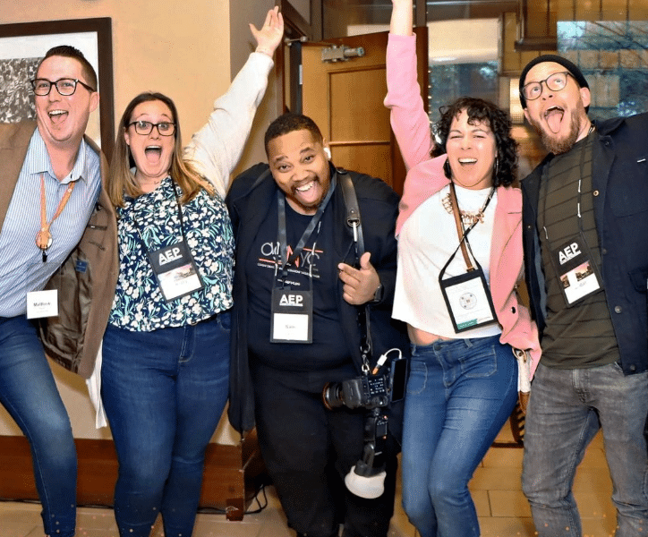 A group of excited AEP conference attendees in business casual with their arms raised in celebration.