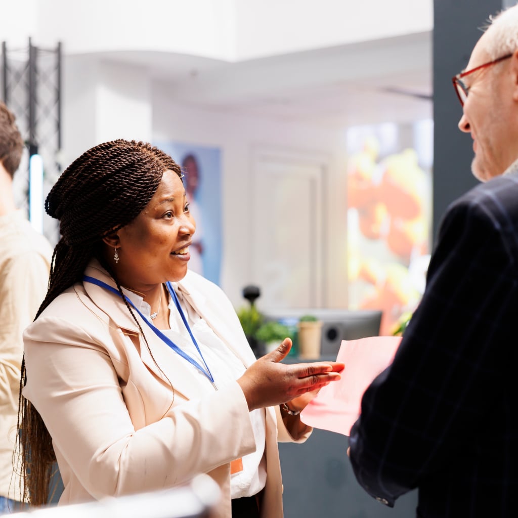 A woman dressed in business attire speaking to a colleague about information on a piece of paper.